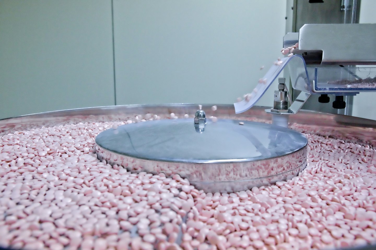 Light pink pills pour from a chute into a metal bin.