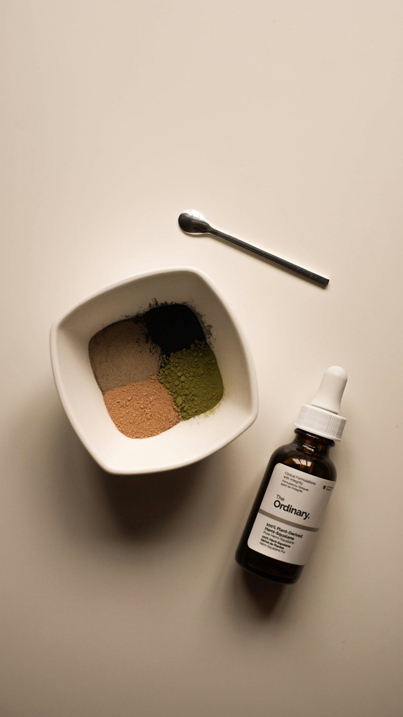 Skincare powders in a divided bowl with dropper and spoon.